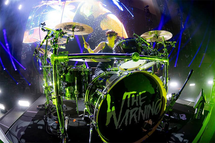 A woman plays a set of drums labelled "The Warning," to represent one of the best Mexican music or podcasts that MND staff discovered in 2024.