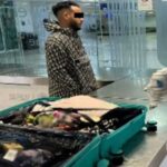 A man stands by an open suitcase in an airport revision area