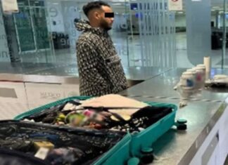 A man stands by an open suitcase in an airport revision area