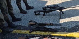 High caliber automatic rifles laid in a row on a street in Mexico. In view nearby are the legs of people in soldier's boots and military fatigues.