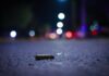 A close up view of a bullet casing lying on a nighttime street with lights in the distance