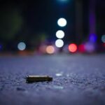 A close up view of a bullet casing lying on a nighttime street with lights in the distance