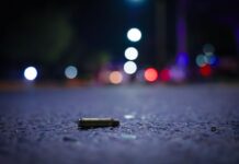 A close up view of a bullet casing lying on a nighttime street with lights in the distance