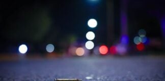 A close up view of a bullet casing lying on a nighttime street with lights in the distance