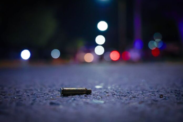 A close up view of a bullet casing lying on a nighttime street with lights in the distance