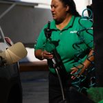 Mexican woman wearing Pemex uniform holding a gas station pump as she prepares to put it into a car's gas tank.