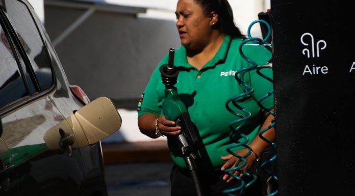 Mexican woman wearing Pemex uniform holding a gas station pump as she prepares to put it into a car's gas tank.