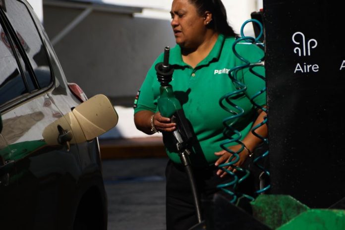 Mexican woman wearing Pemex uniform holding a gas station pump as she prepares to put it into a car's gas tank.