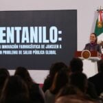 Mexico's President Claudia Sheinbaum standing at the presidential podium and in front of a projection screen with large white letters.