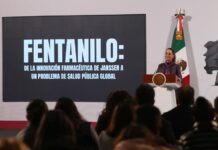 Mexico's President Claudia Sheinbaum standing at the presidential podium and in front of a projection screen with large white letters.