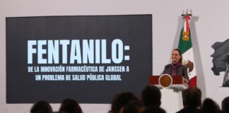 Mexico's President Claudia Sheinbaum standing at the presidential podium and in front of a projection screen with large white letters.