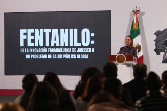 Mexico's President Claudia Sheinbaum standing at the presidential podium and in front of a projection screen with large white letters.