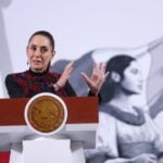Claudia Sheinbaum at a press conference, standing behind the presidential podium, gesturing with both hands parallel in front of her, as if to show the size of something.