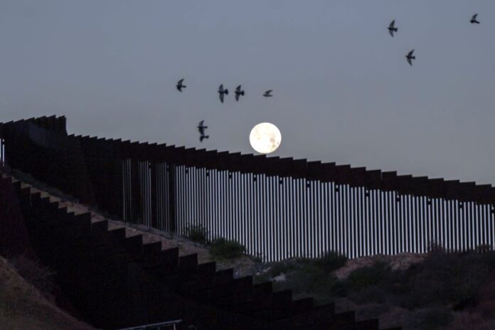 A full moon rises over the Mexico-U.S. border wall