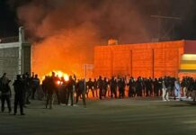 Security officials stand siloutted against the flames of a burning migrant encampment after a raid in Chihuahua went wrong