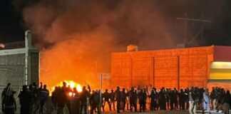 Security officials stand siloutted against the flames of a burning migrant encampment after a raid in Chihuahua went wrong