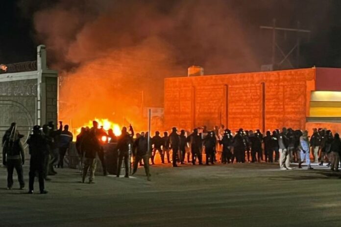 Security officials stand siloutted against the flames of a burning migrant encampment after a raid in Chihuahua went wrong