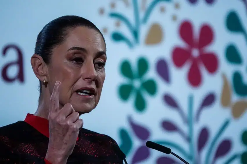 President Claudia Sheinbaum at a press conference, holding her index finger up while answering a reporter's question