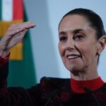 President Claudia Sheinbaum at a press conference. She has her right hand raised to eye level as she makes a point to reporters.