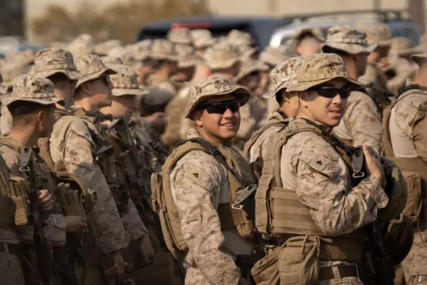 A group of US soldiers in brown duty fatigues at the U.S.-Mexico border. Two are looking at the camera and are wearing sunglasses.