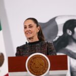 Mexico's President Claudia Sheinbaum standing at the presidential podium in the National Palace during a press conference.