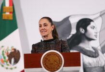 Mexico's President Claudia Sheinbaum standing at the presidential podium in the National Palace during a press conference.