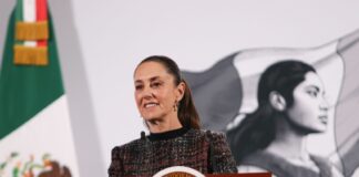 Mexico's President Claudia Sheinbaum standing at the presidential podium in the National Palace during a press conference.