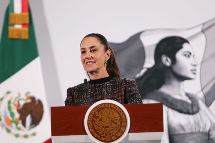 Mexico's President Claudia Sheinbaum standing at the presidential podium in the National Palace during a press conference.