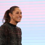 President Claudia Sheinbaum in a dark multicolored sweater smiling at reporters during a press conference at the National Palace press briefing room