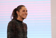 President Claudia Sheinbaum in a dark multicolored sweater smiling at reporters during a press conference at the National Palace press briefing room