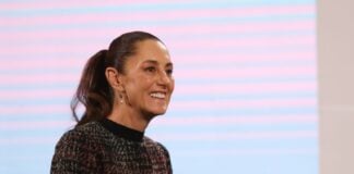 President Claudia Sheinbaum in a dark multicolored sweater smiling at reporters during a press conference at the National Palace press briefing room