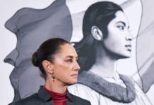 Side profile photo of Mexican President Claudia Sheinbaum at a press conference, standing in a parallel position to her admnistration's logo, a illustration in profile of a young Mexican Indigenous woman standing in front of the Mexican flag