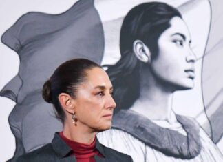 Side profile photo of Mexican President Claudia Sheinbaum at a press conference, standing in a parallel position to her admnistration's logo, a illustration in profile of a young Mexican Indigenous woman standing in front of the Mexican flag