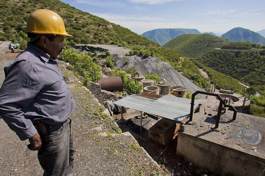 A miner in a hard hat looks over a landscape including a mine