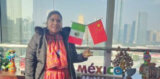 Lorena Ramirez posing while standing in a traditional Raramuri dress and holding small flags from Mexico and China.