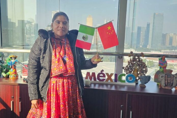 Lorena Ramirez posing while standing in a traditional Raramuri dress and holding small flags from Mexico and China.