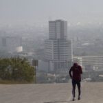 A runner jogs on a smoggy day in Monterrey, Nuevo León, with the city skyline behind them.