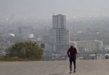 A runner jogs on a smoggy day in Monterrey, Nuevo León, with the city skyline behind them.