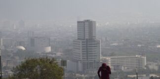 A runner jogs on a smoggy day in Monterrey, Nuevo León, with the city skyline behind them.
