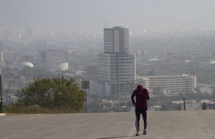 A runner jogs on a smoggy day in Monterrey, Nuevo León, with the city skyline behind them.