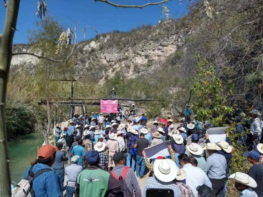 Mexican men in tee shirts, button down shirts, many of them in cowboy hats, gathered in a crowd on a bridge over small river in Jamauve, Tamaulipas