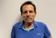 Mugshot of Sinaloa Cartel cofounder Ismael "El Mayo" Zambada, wearing a blue Boss brand polo shirt as he stares into the camera unsmiling