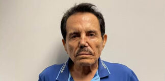 Mugshot of Sinaloa Cartel cofounder Ismael "El Mayo" Zambada, wearing a blue Boss brand polo shirt as he stares into the camera unsmiling