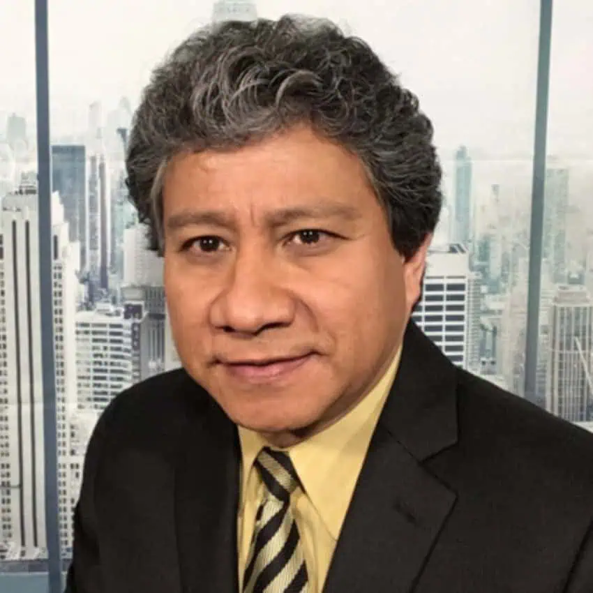 Posed photo of Moody's Director of Economic Analysis for Latin America Alfredo Coutiño in front of a window looking out onto a city skyline.