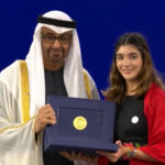 A man wearing a ghutra head covering presents the Zayed environmental award to a young Mexican woman