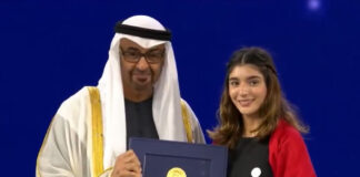 A man wearing a ghutra head covering presents the Zayed environmental award to a young Mexican woman