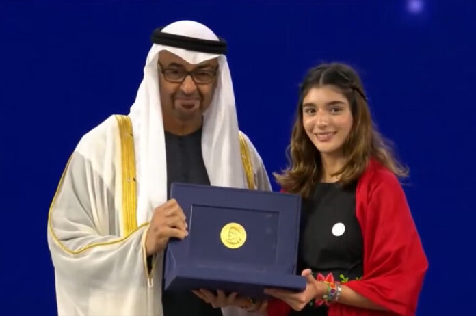 A man wearing a ghutra head covering presents the Zayed environmental award to a young Mexican woman