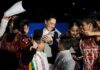 Mexican President Claudia Sheinbaum surrounded by Indigenous young women and children, who are smiling, looking at photos on their phone and clamoring for autographs