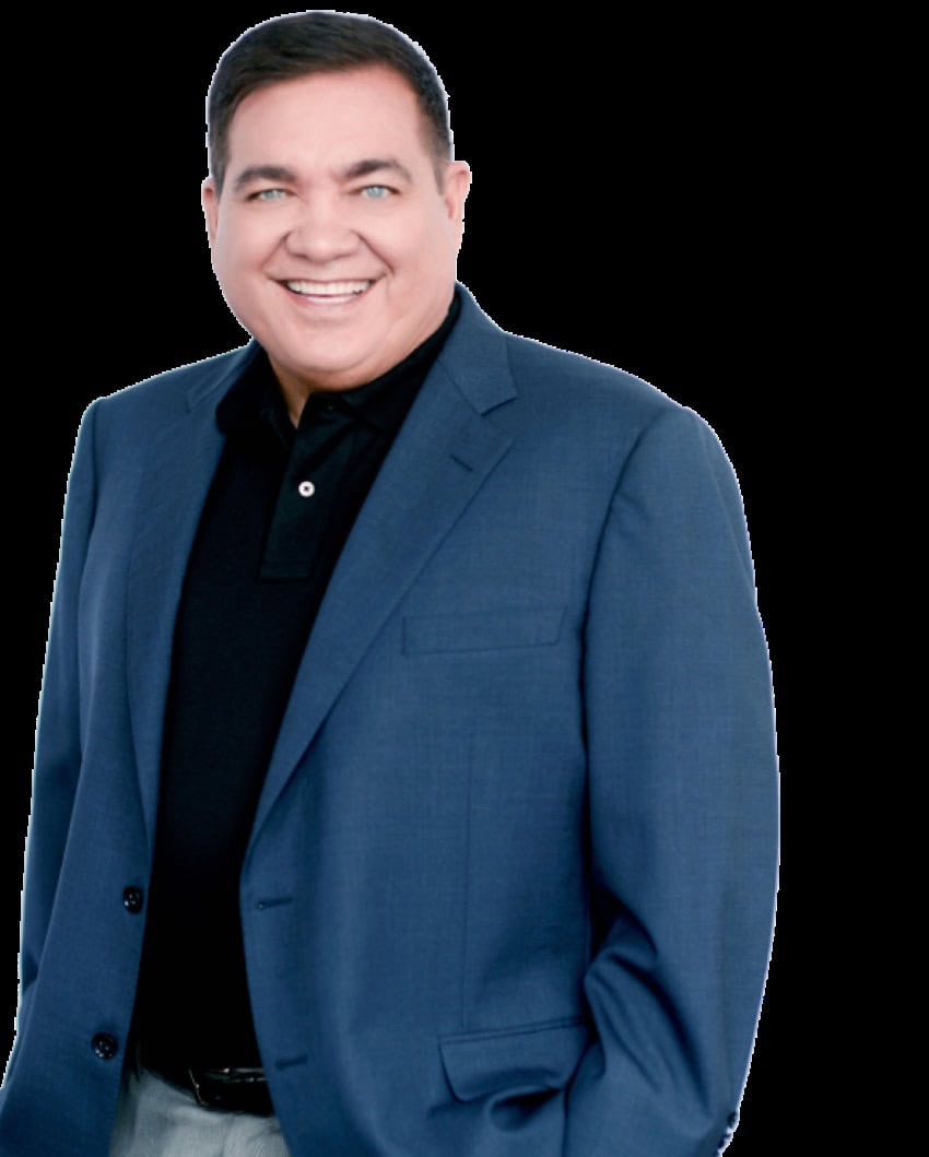 A man with short, dark hair posing in a dark blue suit jacket and black polo shirt, smiling for a publicity photo