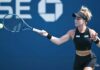 Mexican professional tennis player Renata Zarazua in a black tennis outfit and her blonde hair tired up in a bun, hitting a tennis ball with a forehand swing during a match.